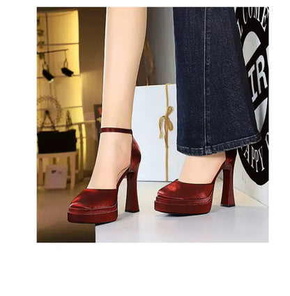 Red high-heeled shoes worn with denim jeans in an indoor setting.