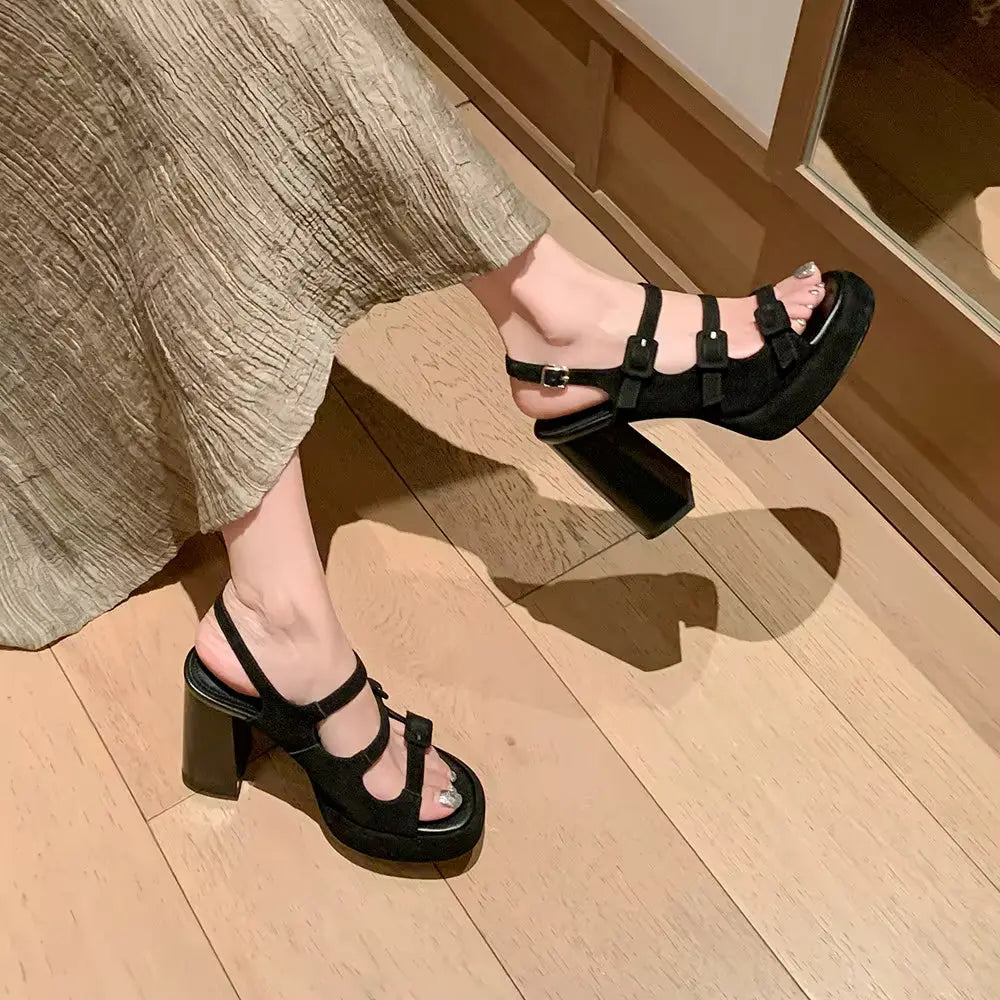 Black platform sandals worn on a wooden floor