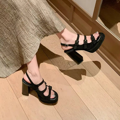 Black platform sandals worn on a wooden floor