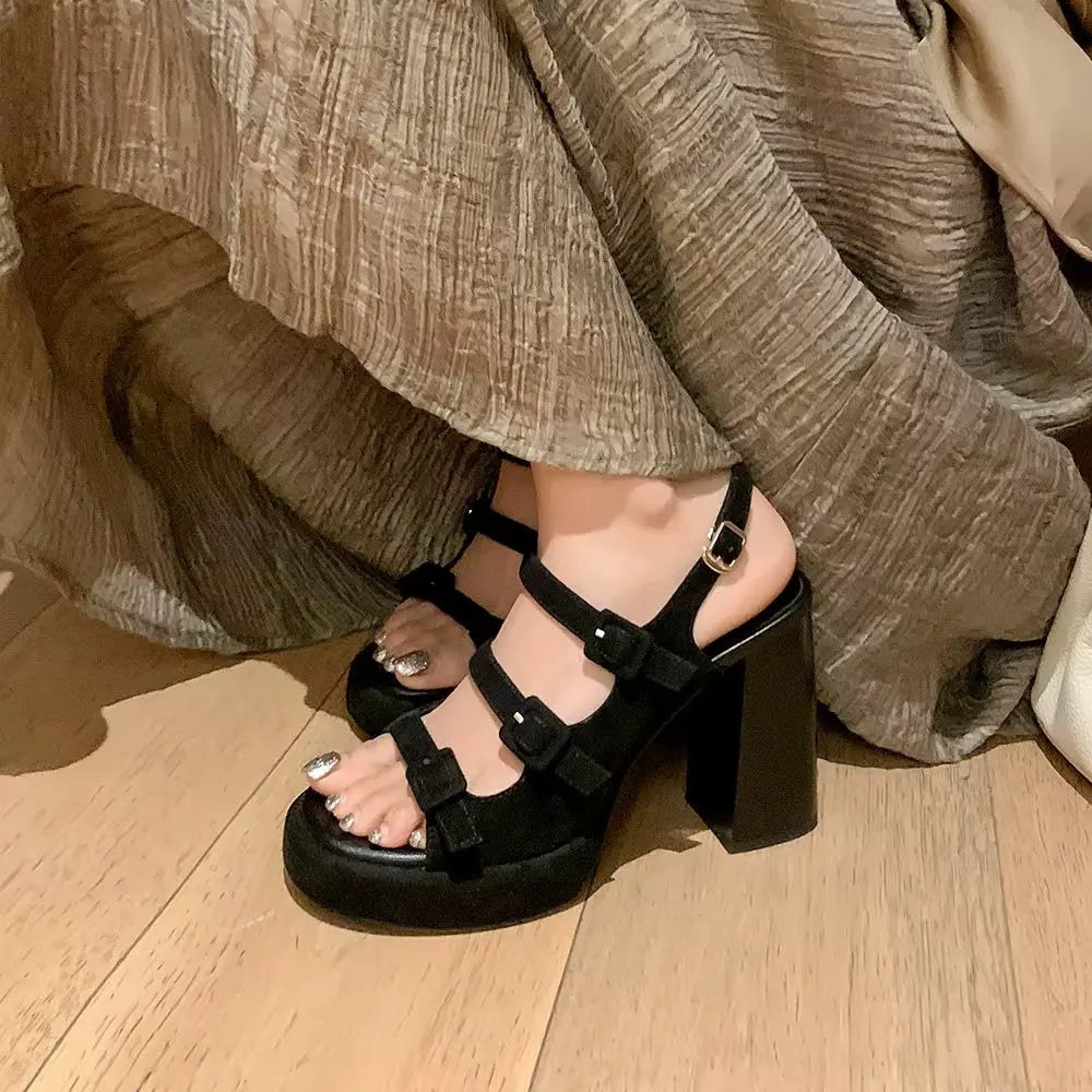 Black platform sandals worn with a beige outfit on a wooden floor.