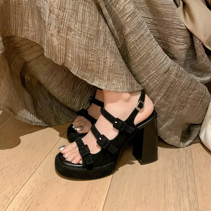 Black platform sandals worn with a beige outfit on a wooden floor.