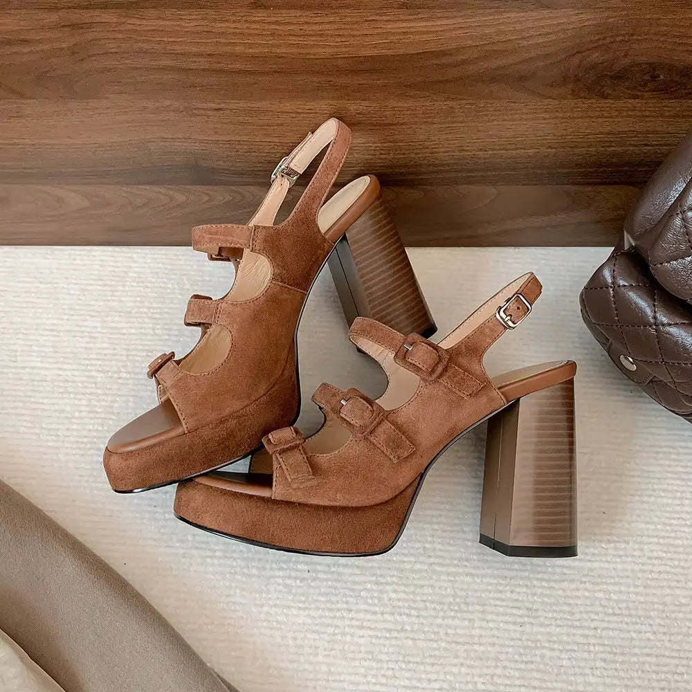 Brown suede platform sandals with wooden block heels on a textured surface.