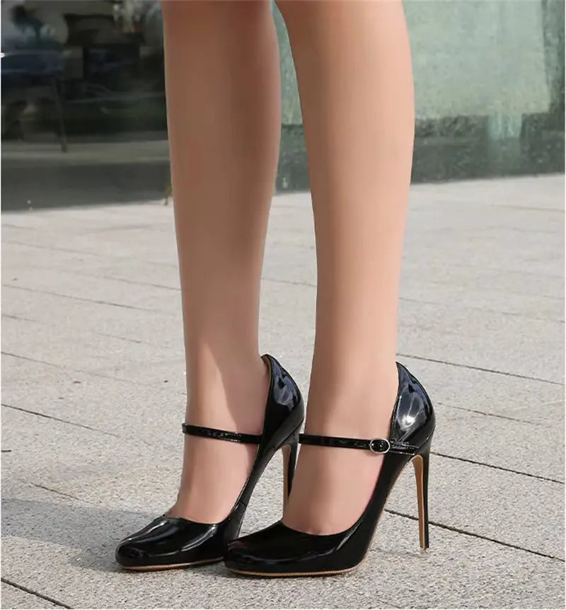 Black high-heeled shoes with thin straps worn by a person on a pavement.